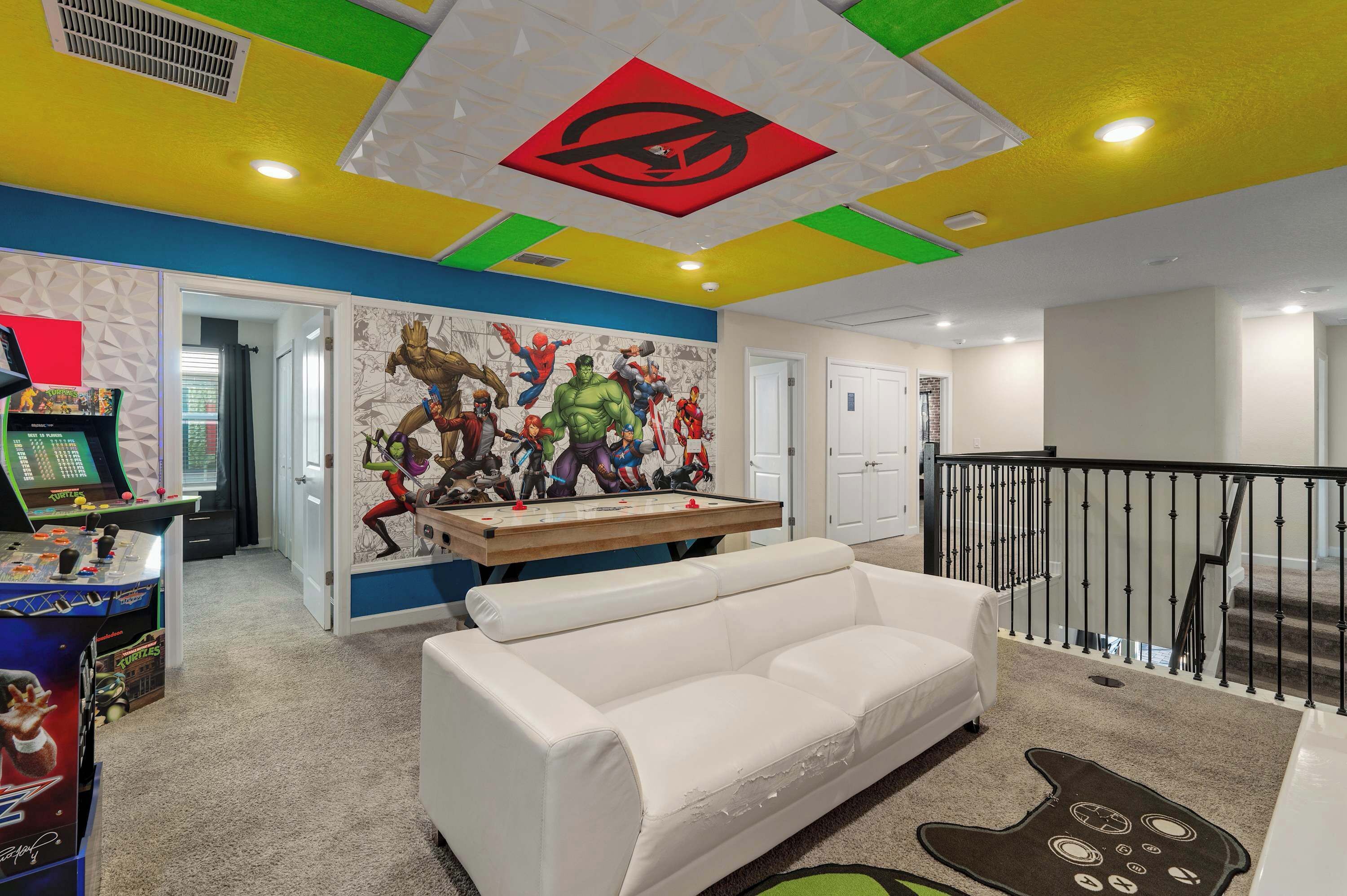 Une pièce avec un canapé blanc, une table de baby-foot et une fresque murale représentant des super-héros.