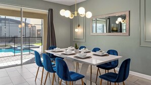 A dining area with a white table set for six, blue chairs, a large mirror, and a pool view.