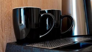 En kaffemaskine med to sorte kopper på en bordplade.