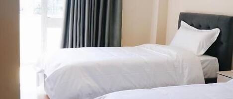 A hotel room with two beds, a large window with curtains, and a view of the outdoors.