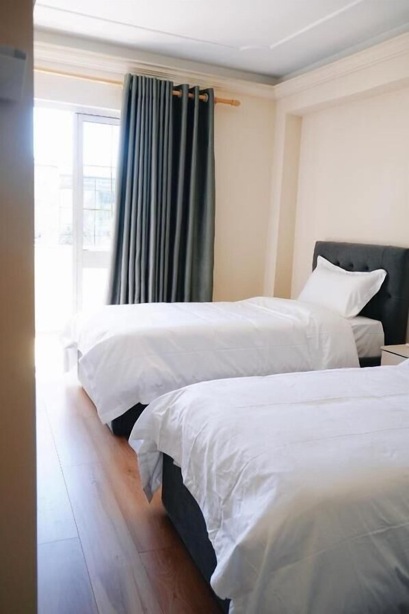 Habitación de hotel con dos camas, un ventanal con cortinas y vistas al exterior.