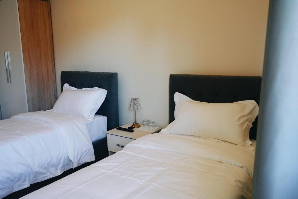 Een hotelkamer met twee eenpersoonsbedden, een nachtkastje met een lamp en een kledingkast.