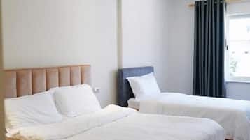 Two single beds with white linens, a large window, and light-colored flooring.