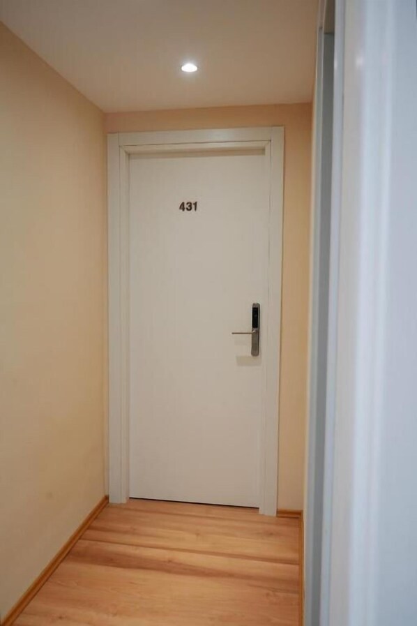 Un pasillo estrecho con una puerta blanca marcada con el número 431 y un picaporte de metal.