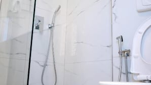 Et moderne badeværelse med en brusekabine i glas, et hvidt marmorgulv og en hvid vask.