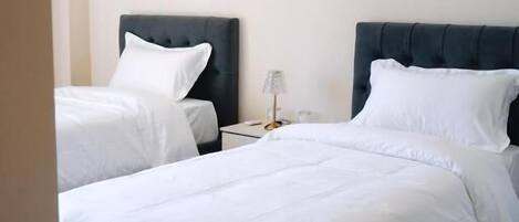 Habitación de hotel con dos camas, cada una con cabecero oscuro y ropa de cama blanca.