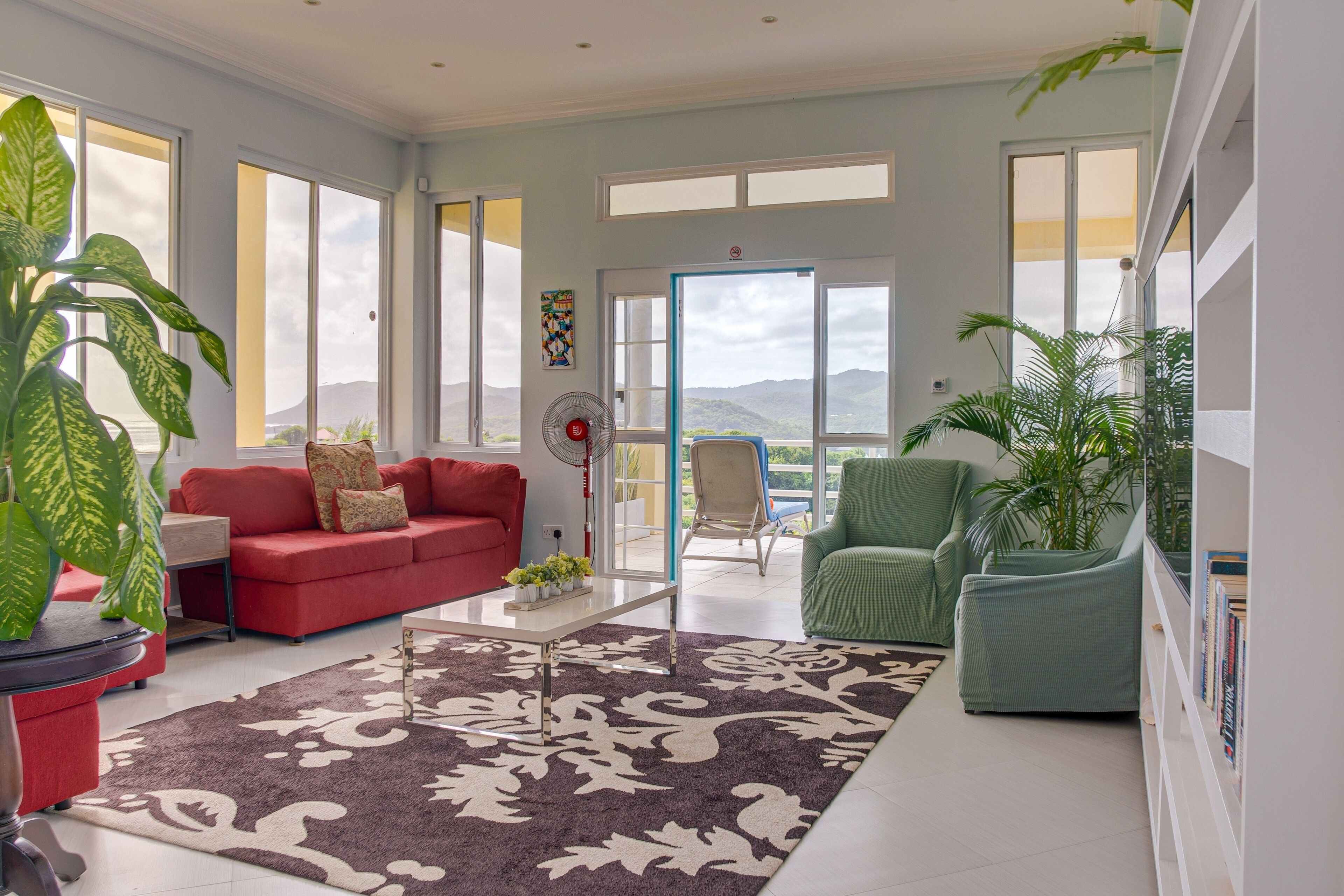 A spacious living room with a red sofa, green armchair, and a large window offering a view of the mountains.