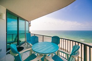 Un balcon avec une table et des chaises, une vue sur l’océan et un ciel dégagé.