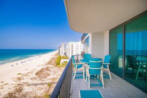 A balcony with a view of the beach, a table with chairs, and a glass door.