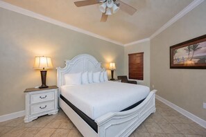 A bedroom with a bed, two bedside tables with lamps, a ceiling fan, a window with blinds, and a painting on the wall.