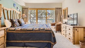 A bedroom with a large bed, a wooden headboard, a TV, a desk, and a view of the outdoors. - 5023 Gateway 2 Bedroom Condo (Keystone)