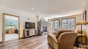 A spacious living room with a stone fireplace, leather sofas, and a flat-screen TV on a wooden cabinet. - 5023 Gateway 2 Bedroom Condo (Keystone)