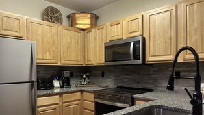 A kitchen with wooden cabinets, a stainless steel refrigerator, a microwave, a coffee maker, and a sink. - 5023 Gateway 2 Bedroom Condo (Keystone)