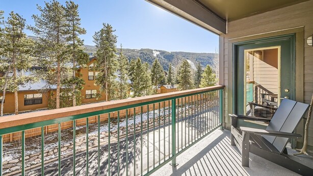 A balcony with a view of a mountainous landscape, a wooden deck, and a chair. - 5023 Gateway 2 Bedroom Condo (Keystone)