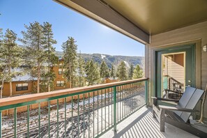 A balcony with a view of a mountainous landscape, a wooden deck, and a chair.