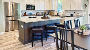 A modern kitchen with white cabinets, stainless steel appliances, a central island with bar stools, and pendant lighting. - Lilys Pad Home with Gourmet Kitchen, Near Beach (Cape Charles)