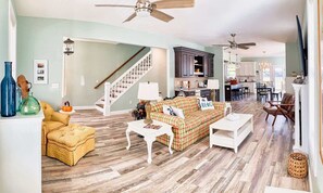 A spacious living room with a wooden floor, a staircase, and a kitchen in the background. - Lilys Pad Home with Gourmet Kitchen, Near Beach (Cape Charles)