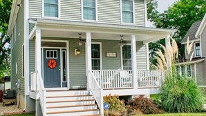 A two-story house with a front porch, a small entryway, and a visible address sign. - Lilys Pad Home with Gourmet Kitchen, Near Beach (Cape Charles)