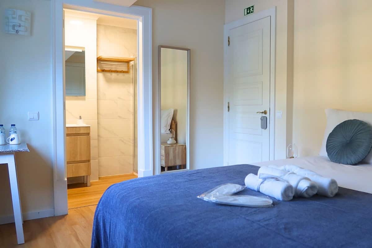 Een hotelkamer met een bed, een nachtkastje met een lamp, een badkamer die door een open deur zichtbaar is, en een tafeltje met waterflesjes.