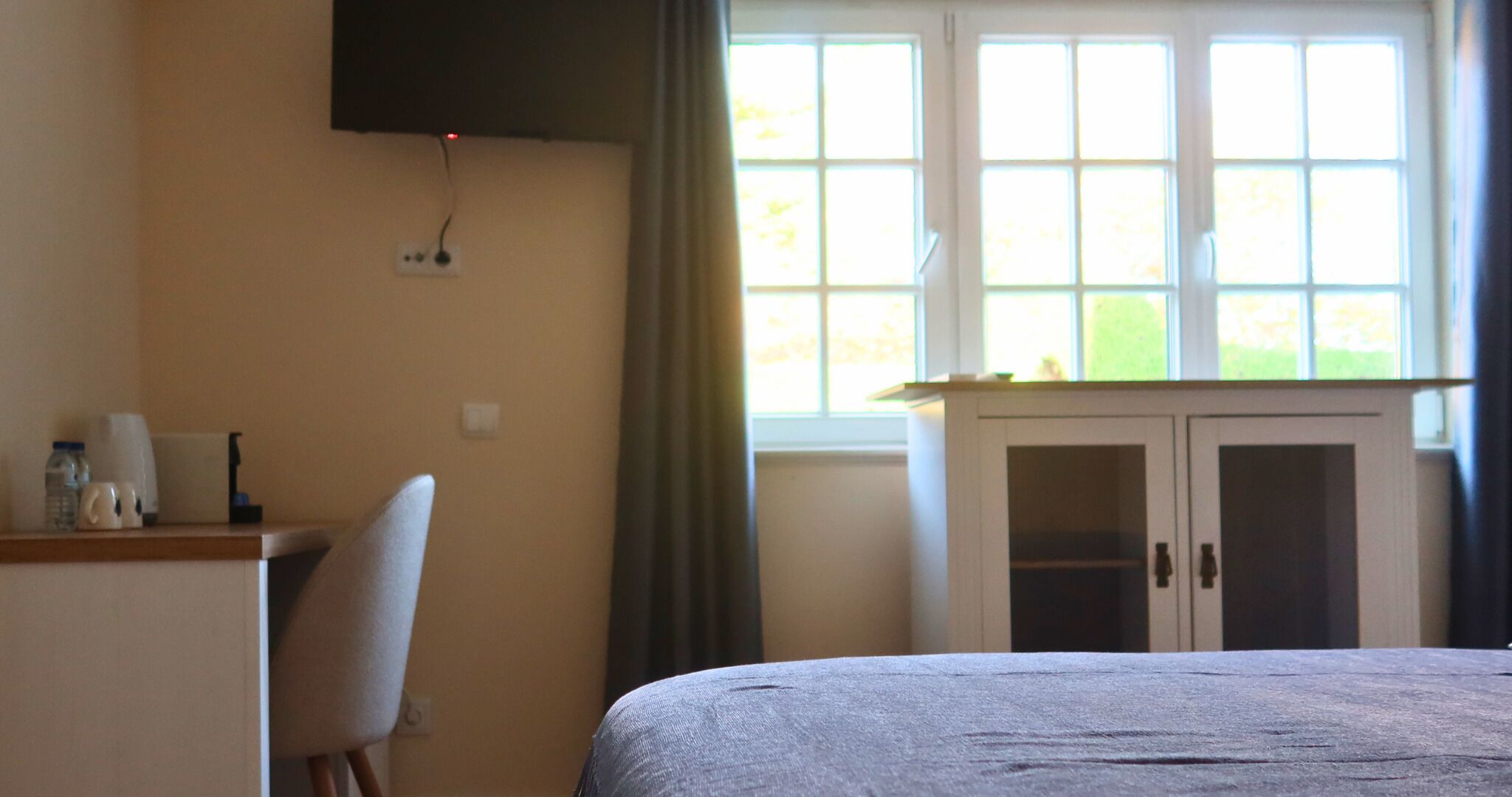 A hotel room with a bed, a desk, a chair, a cabinet, and a window with curtains.