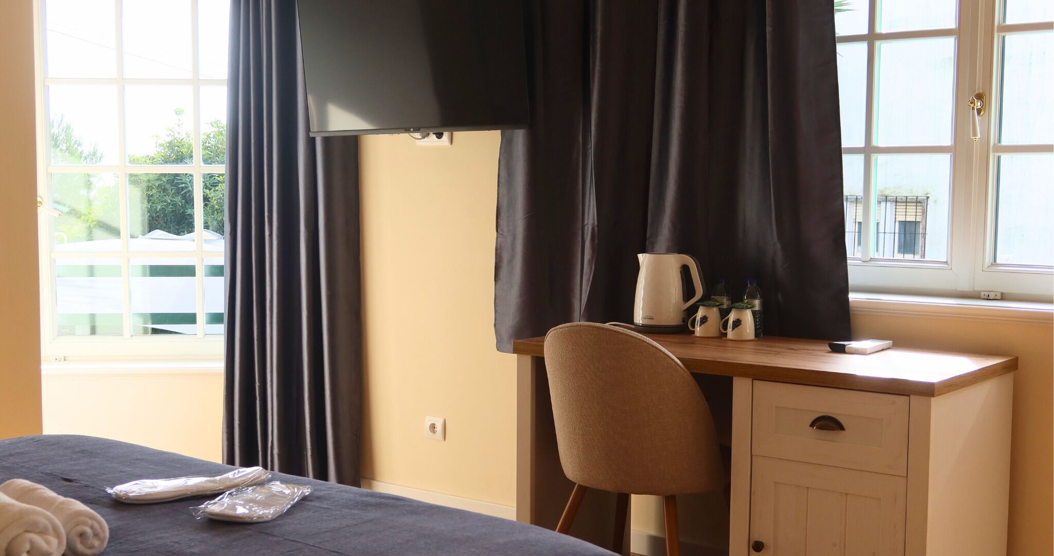 A hotel room with a bed, a desk with a chair, a window with curtains, and a view of the outside.