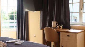 A hotel room with a bed, a desk with a chair, a window with curtains, and a view of the outside.