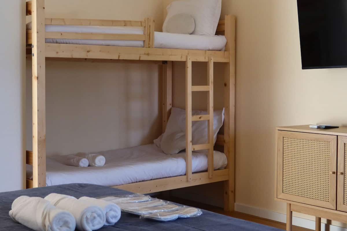 Een slaapkamer met stapelbed, een televisie aan de muur, een houten kast en handdoeken op het bed.