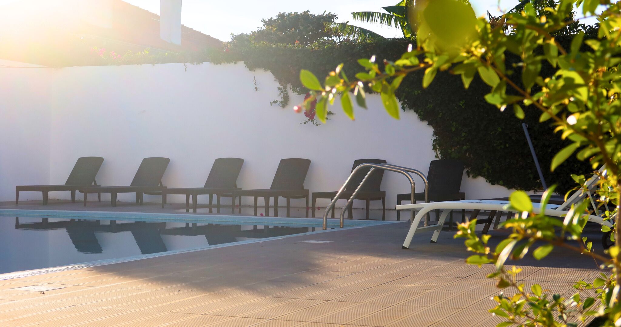 A pool area with lounge chairs and a metal ladder.