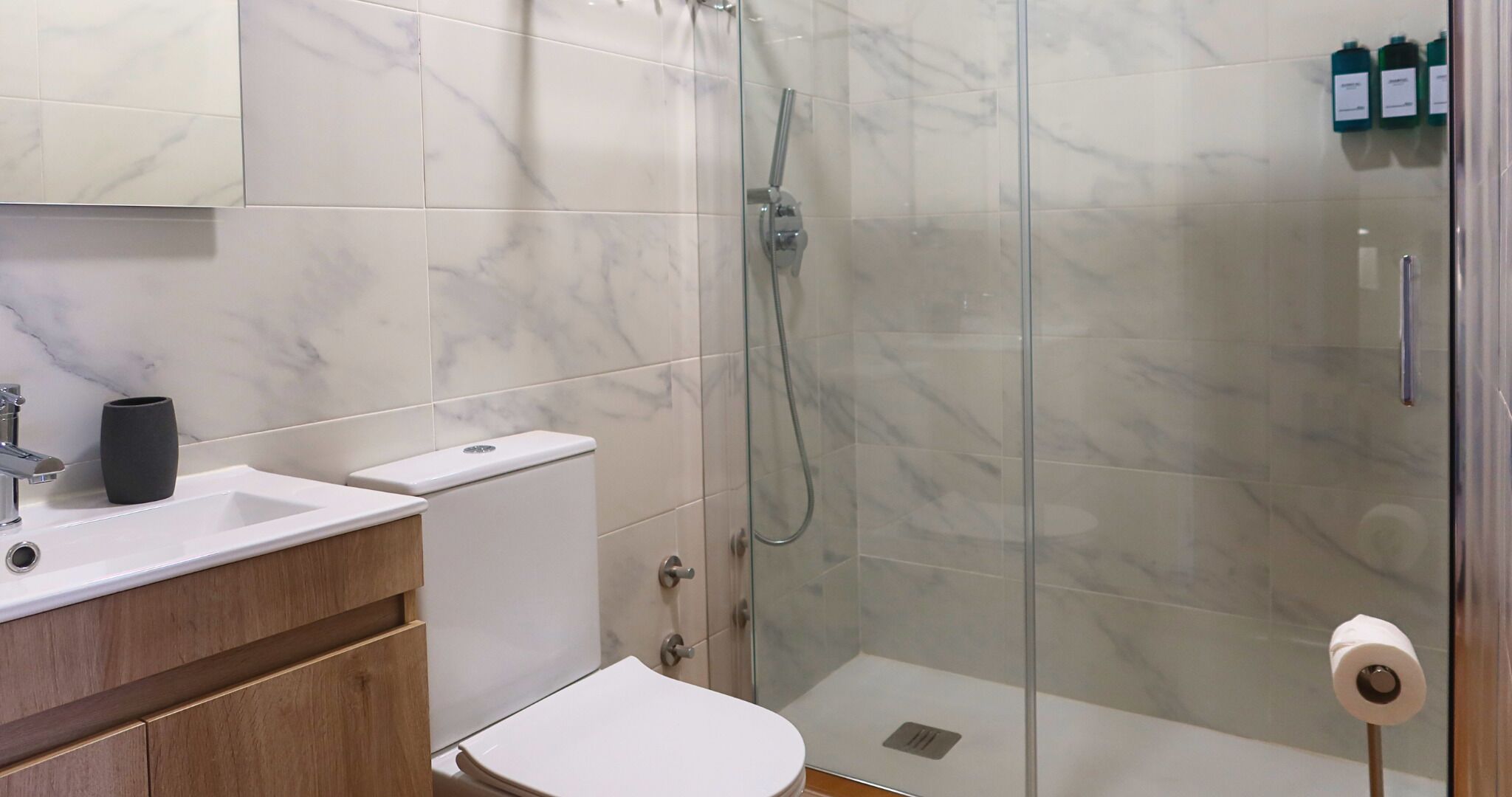 A bathroom with a marble-tiled shower enclosure, a white sink, and a toilet.