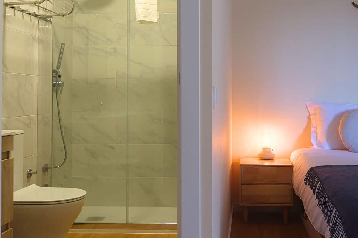 Een badkamer met een douchecabine van glas, een toilet en een nachtkastje met een lamp.