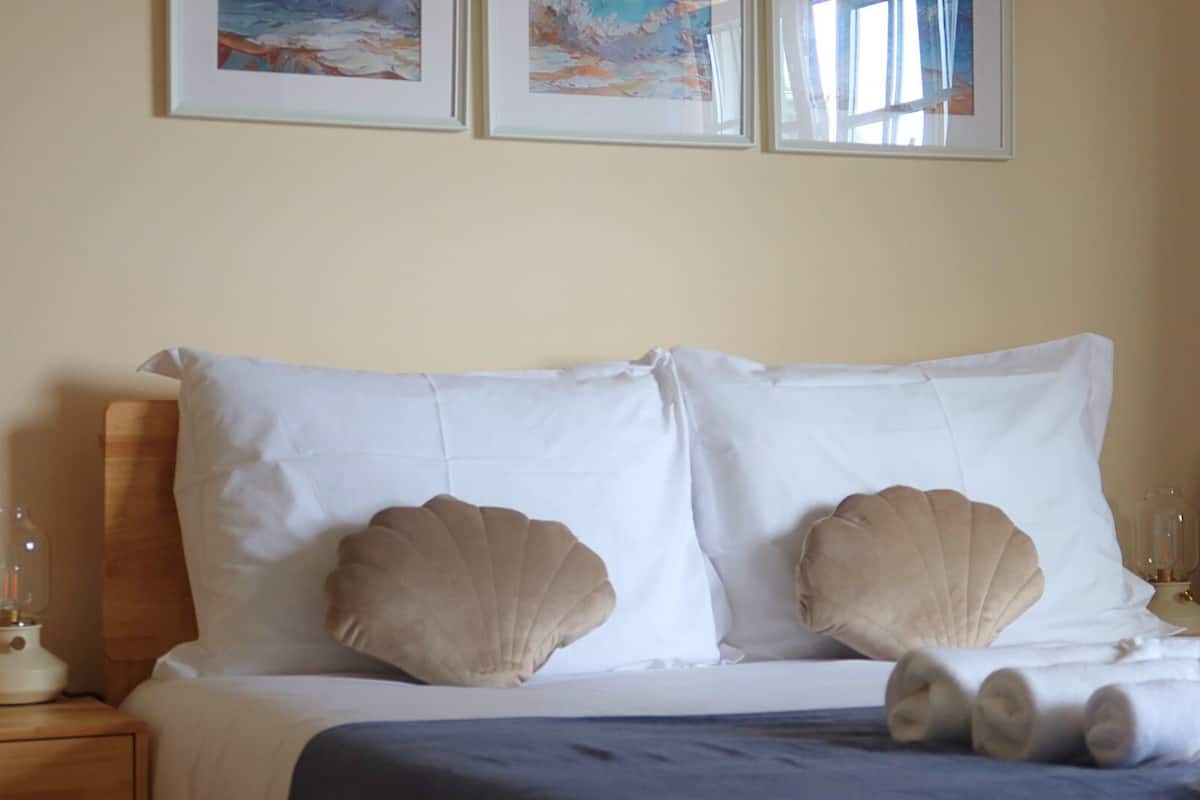 Een netjes opgemaakt bed met twee kussens, een houten hoofdbord en een blauwe deken.