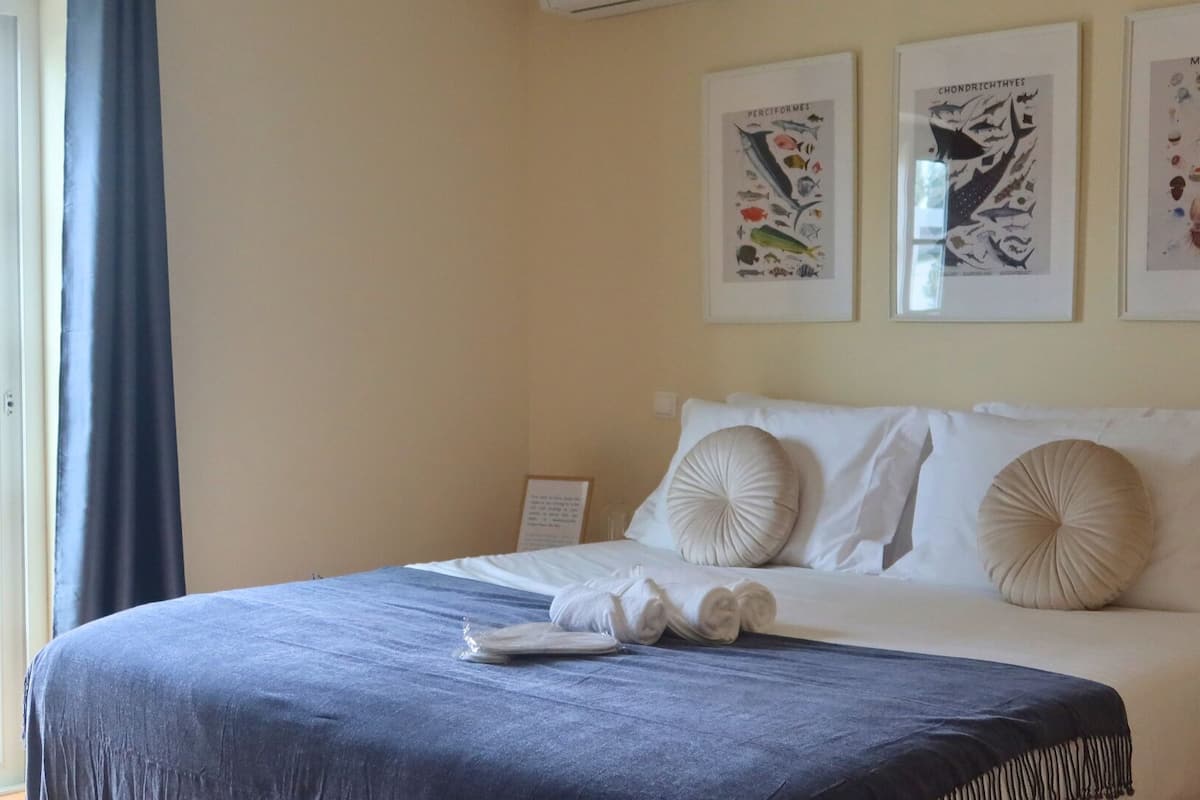 Een netjes opgemaakt bed met een blauwe deken, witte kussens en een lijst met afbeeldingen van zeedieren aan de muur.
