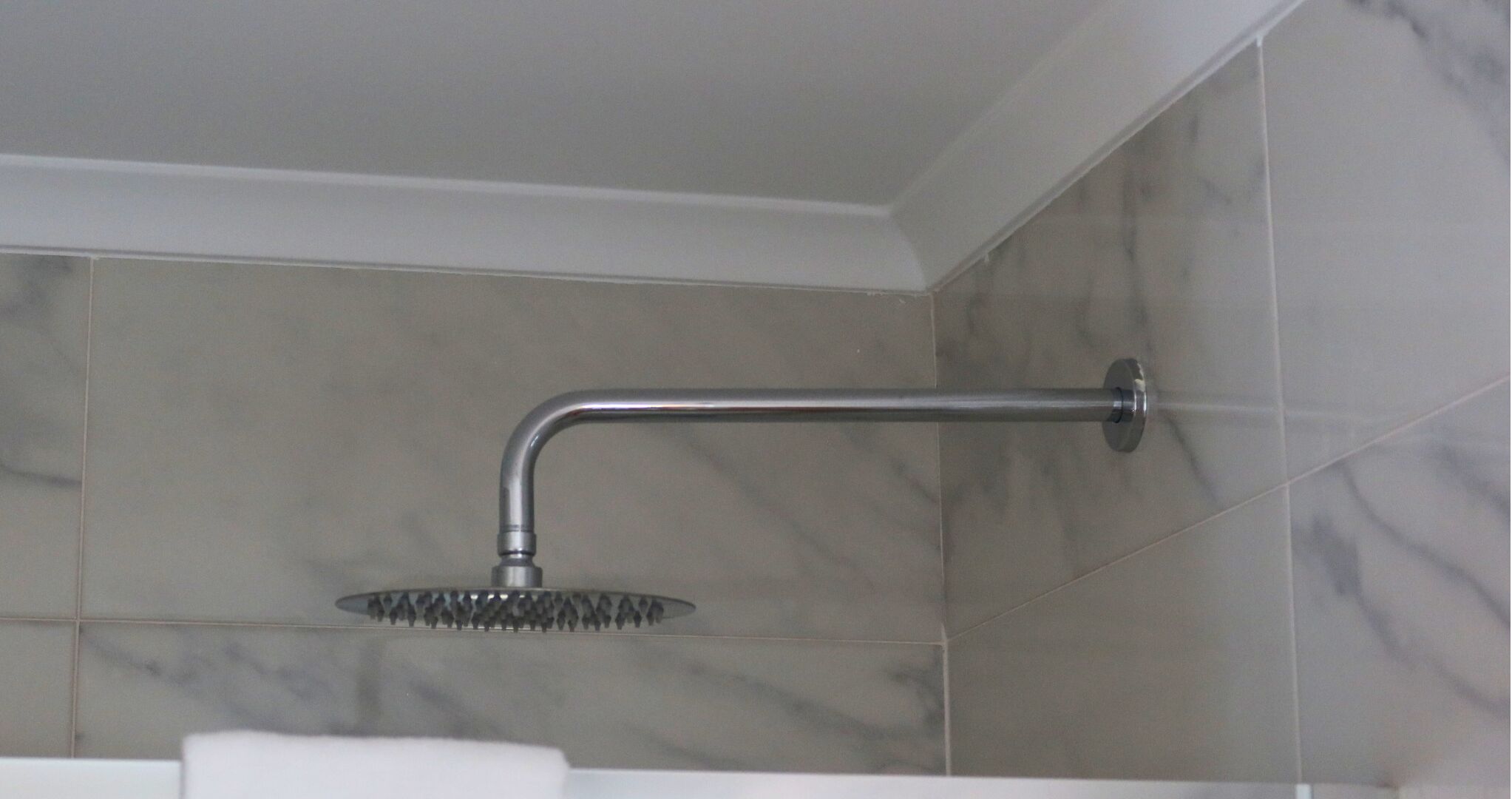 A bathroom with a shower head mounted on a wall, a white sink, and marble tiles.