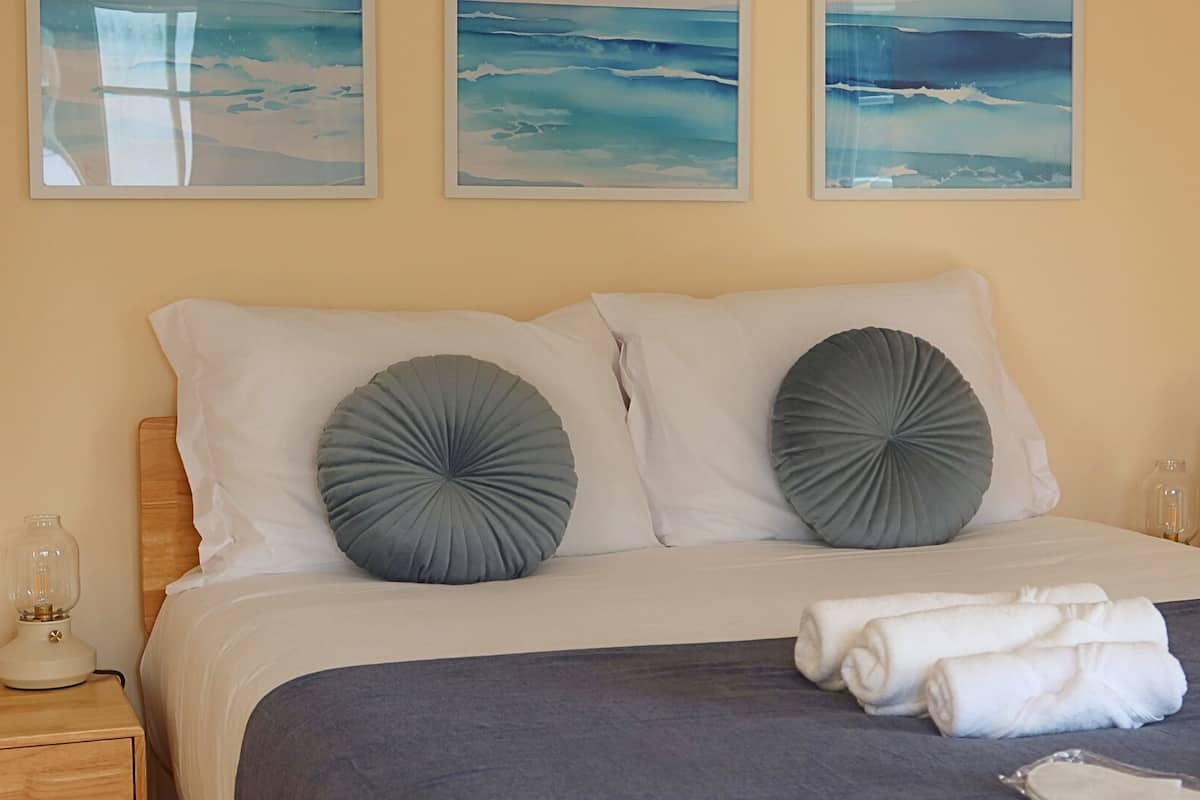 Een netjes opgemaakt bed met twee kussens, een nachtkastje met een lamp, en drie ingelijste kunstwerken aan de muur.