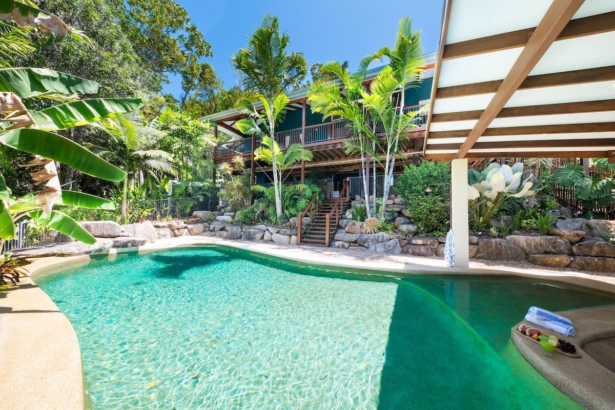 Una piscina cristalina rodeada de plantas tropicales y una estructura de madera de varios niveles.