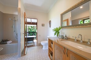 A modern bathroom with a bathtub, shower, and sink. There is a balcony visible through the doorway.