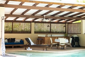A covered outdoor area with a pool, lounge chairs, a bar, and a grill.