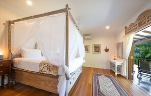 A four-poster bed with a canopy, a bedside table, a small desk, and a view of the outdoors.