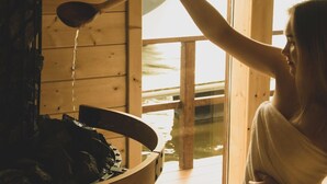 Iemand roert in een pan in een houten hut met uitzicht op een waterlichaam.