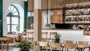 Een restaurant met houten stoelen, een bar met flessen en een groot raam met gordijnen.