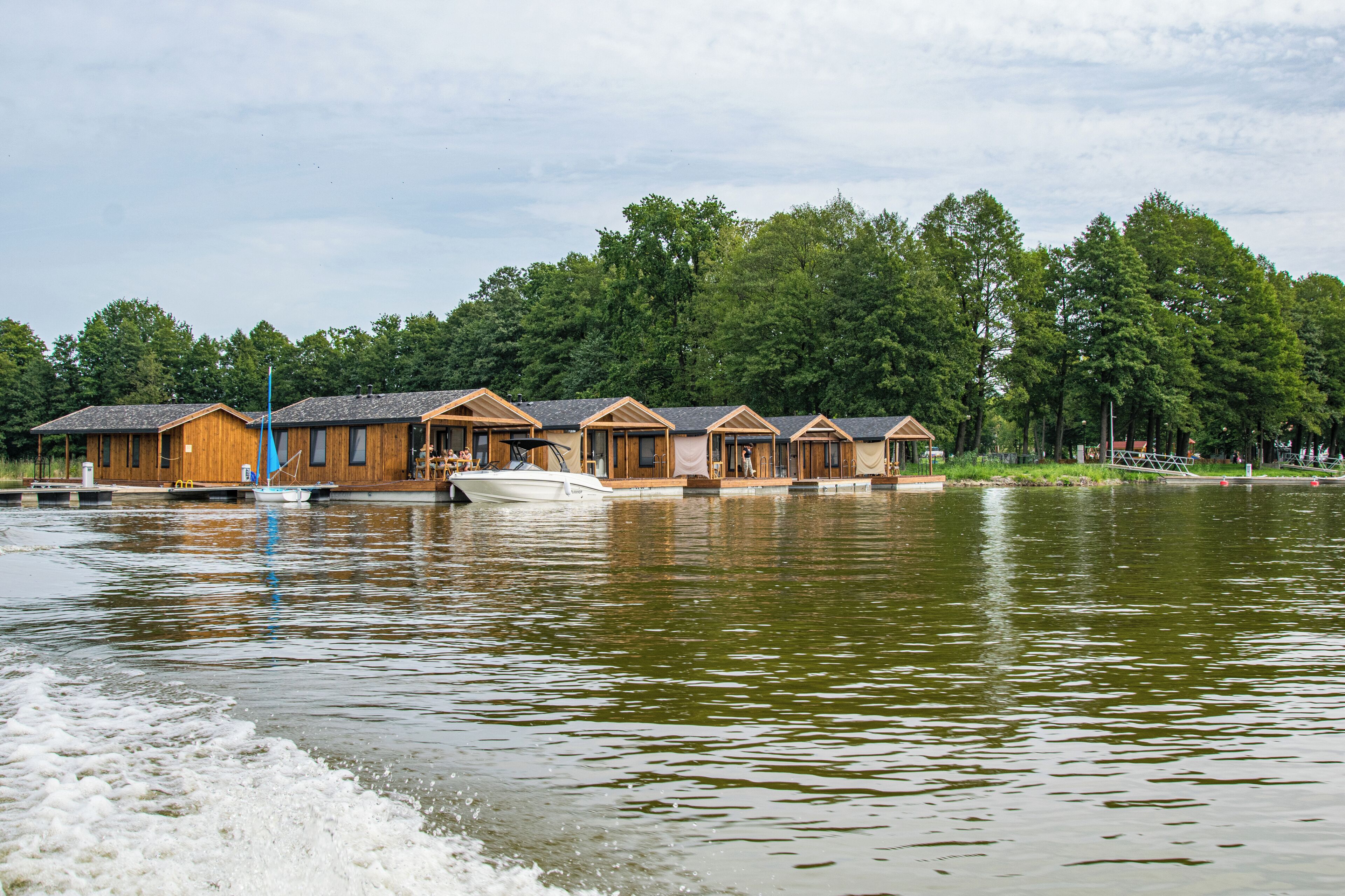 A row of wooden cabins with a dock extending into a calm lake, surrounded by dense trees.