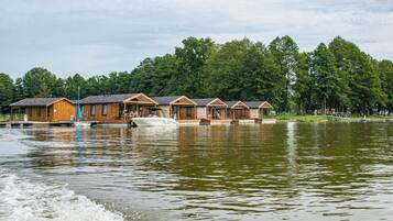 A row of wooden cabins with a dock extending into a calm lake, surrounded by dense trees.
