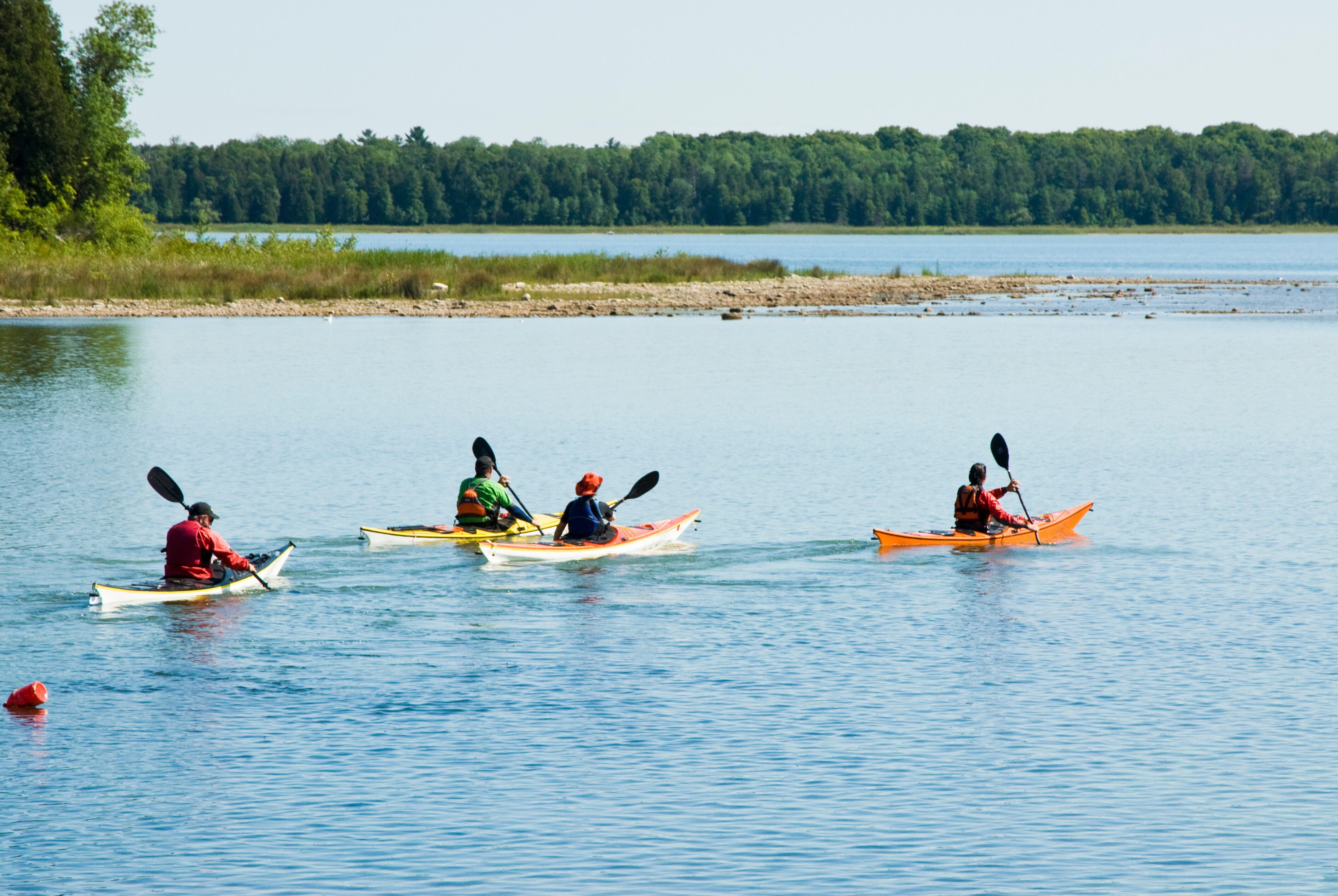 Three kayaks on a calm lake with a forested shoreline.