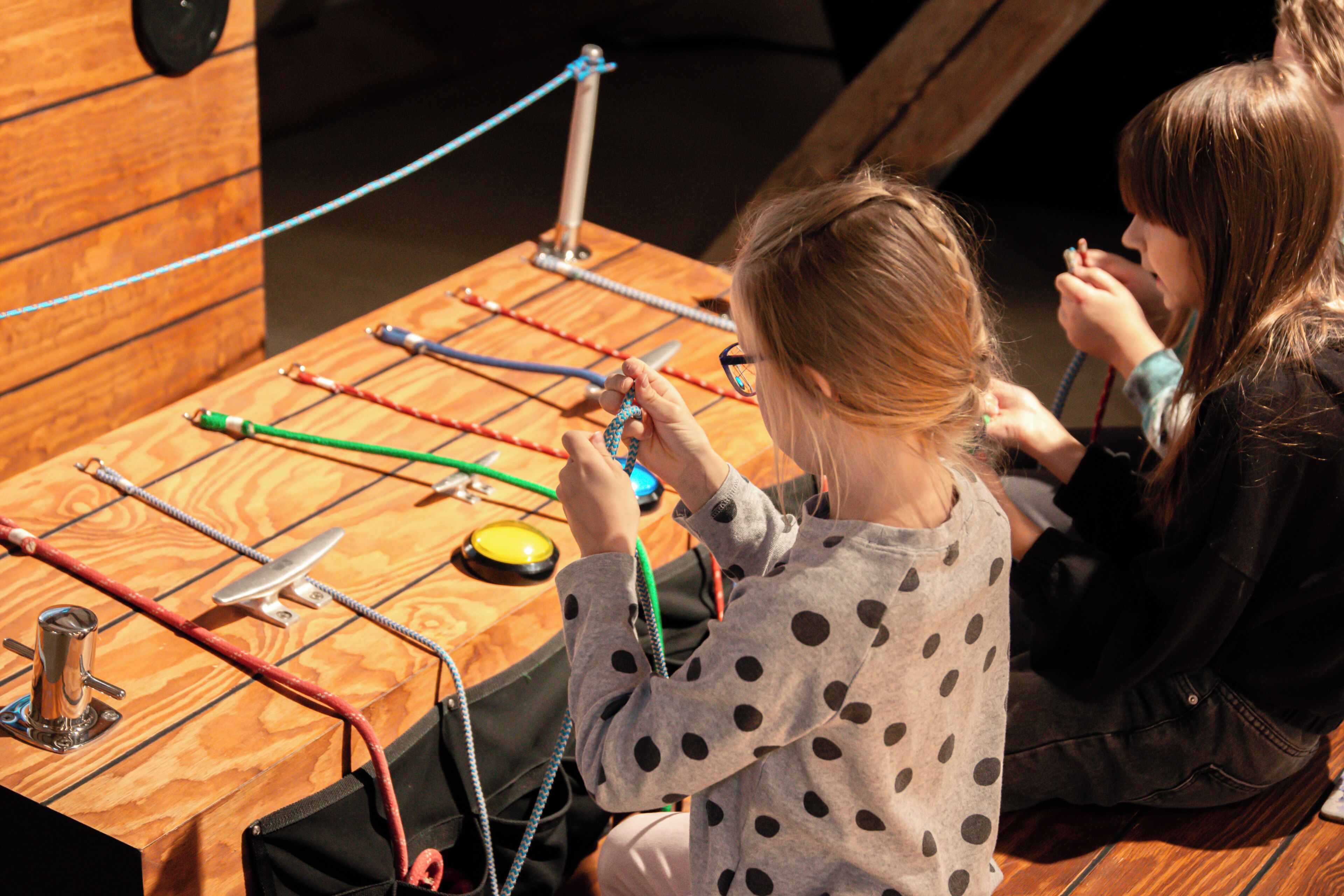 A wooden table with ropes and a metal object, possibly a toy or educational tool.