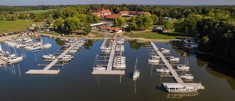 A marina with numerous boats docked at piers, surrounded by greenery and buildings in the background.