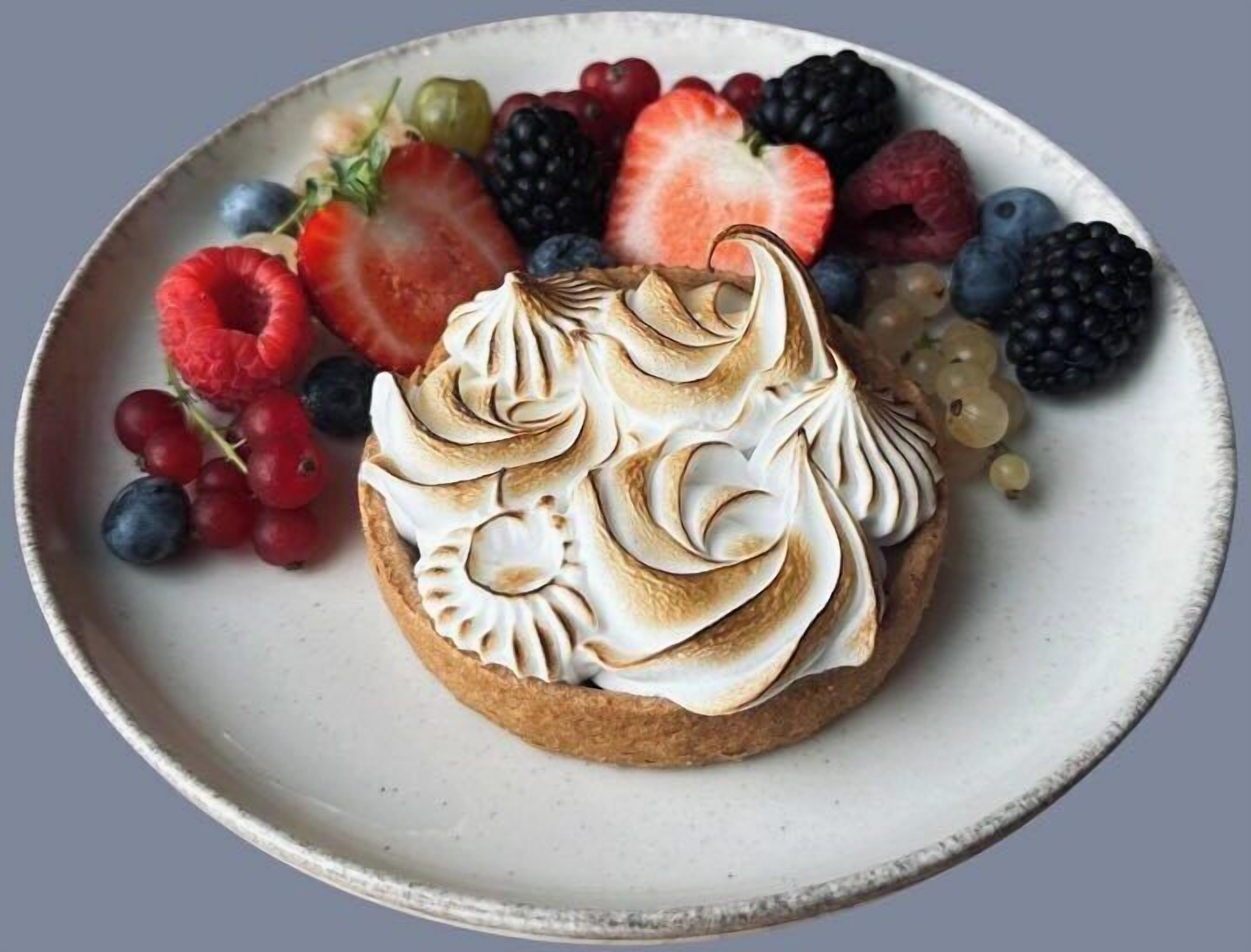 A dessert with meringue on a plate surrounded by various berries.