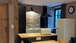 A kitchen with a wooden table, chairs, a toaster, a refrigerator, a brick wall, and a clock on the wall. - Le grand Second, charming gîte for 5 people near Spa town center. (Spa)