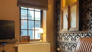 A cozy living room with a stone coffee table, leather sofa, a TV, and a window with a view of a house. - Le grand Second, charming gîte for 5 people near Spa town center. (Spa)