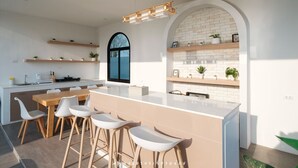 A modern kitchen with white cabinetry, wooden countertops, and bar stools. There are multiple shelves with plants and a large window above the sink. - Oxygen Valley Khao Yai C8 (Pak Chong)