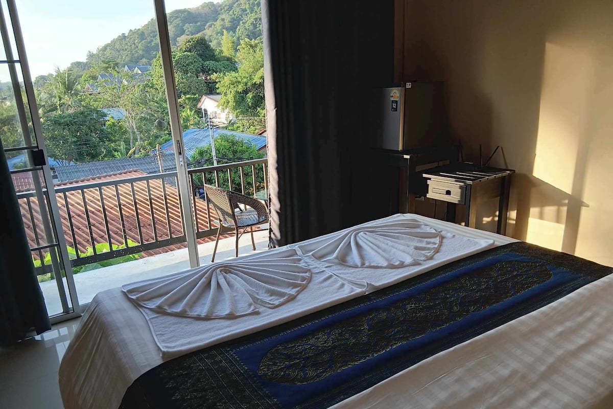 Habitación de hotel con cama, una mesita, una silla y vistas a un paisaje montañoso desde un balcón.